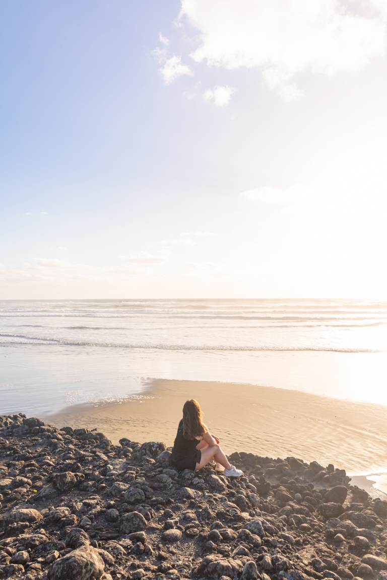 girl sitting watching sunset at Bethells/Te Henga beach