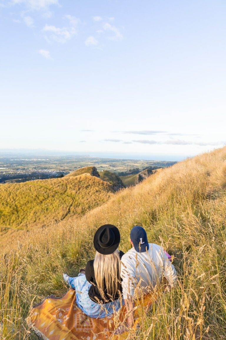 couple sitting on a picnic blanket on the top of te mata peak at golden hour