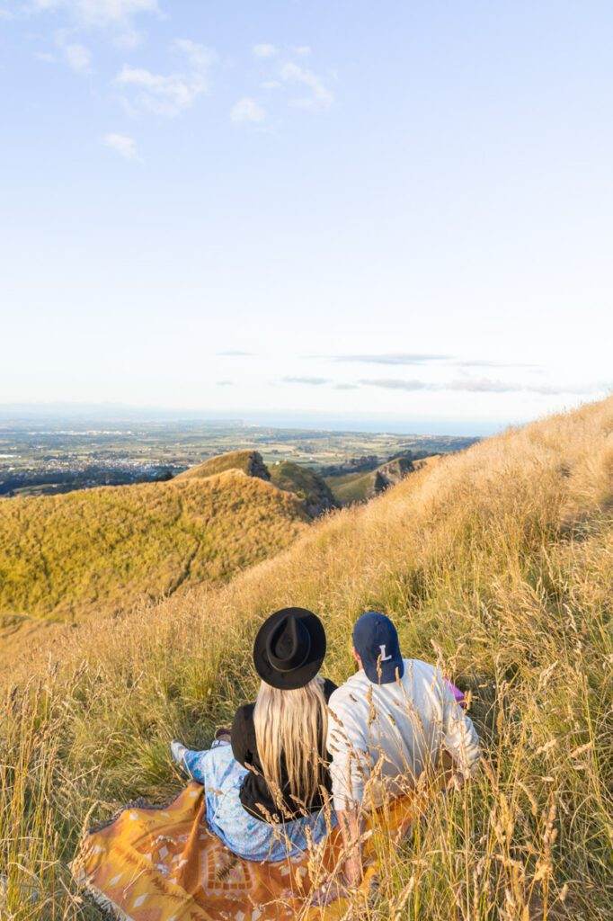 couple sitting on picnic blanket overlooking new zealand landscape