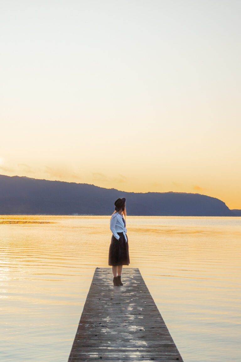 girl standing on lake tarawera boardwalk at sunrise