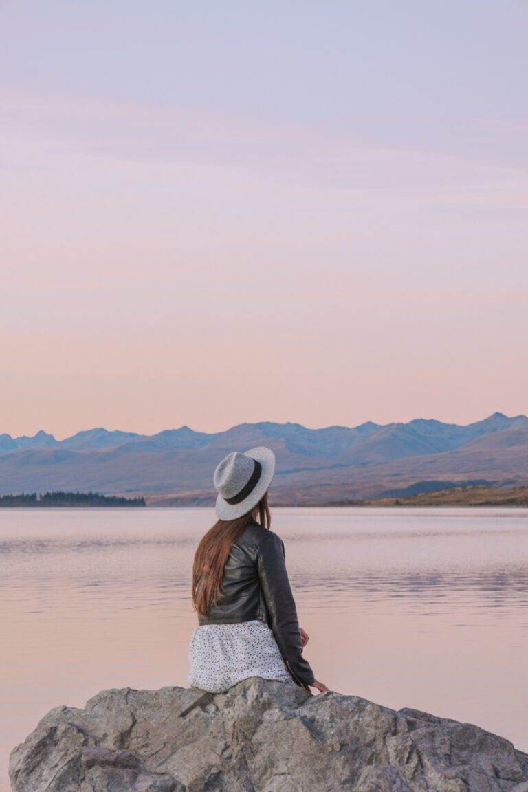 girl sitting at lake tekapo at sunset