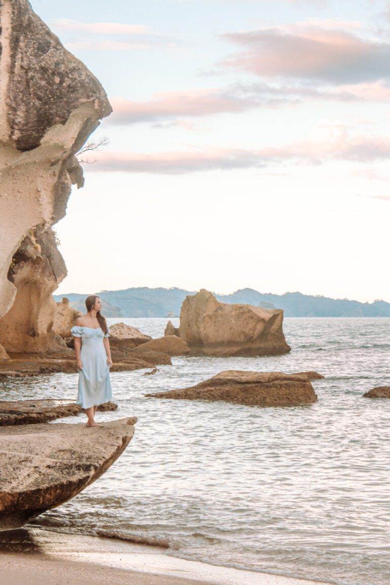 girl standing on rock at lonely bay beach at sunset