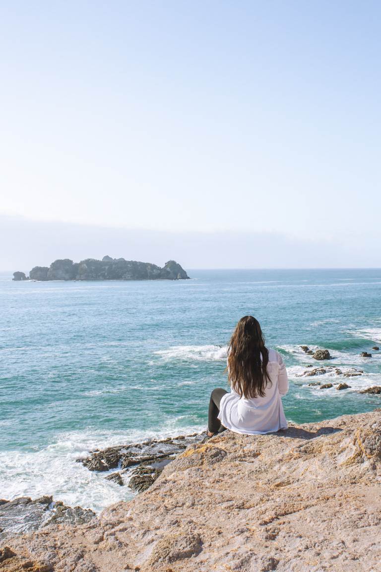 girl sitting on the cliff face of coromandel coast